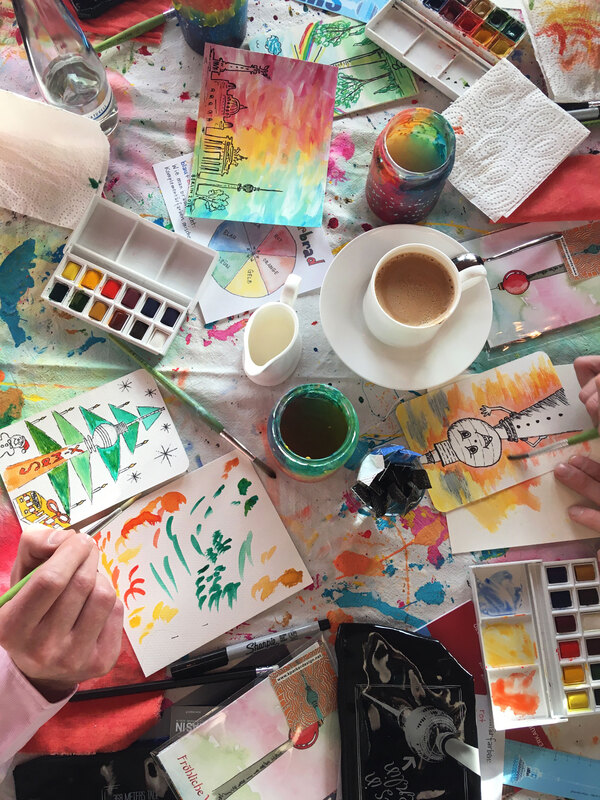 Text: Painting workshops
Image: messy art desk with paintings, watercolors, brushes, and a coffee
